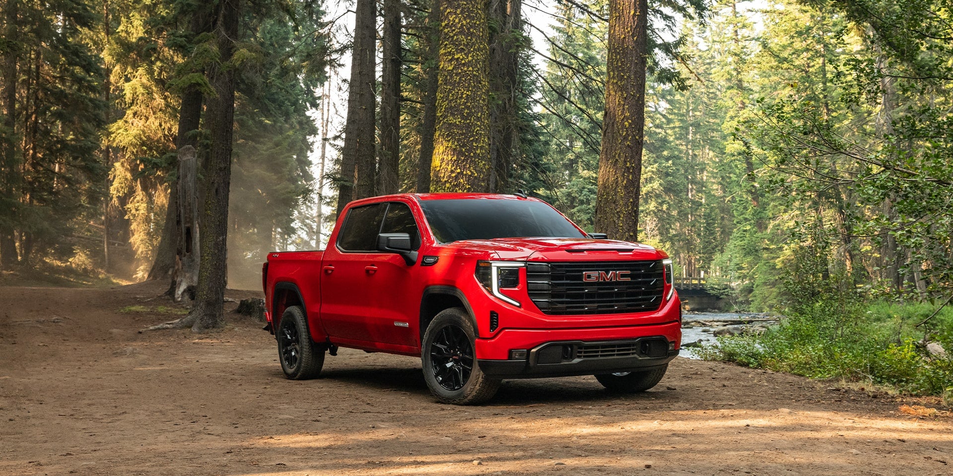 A red GMC Sierra 1500 driving down a dirt road in a forest