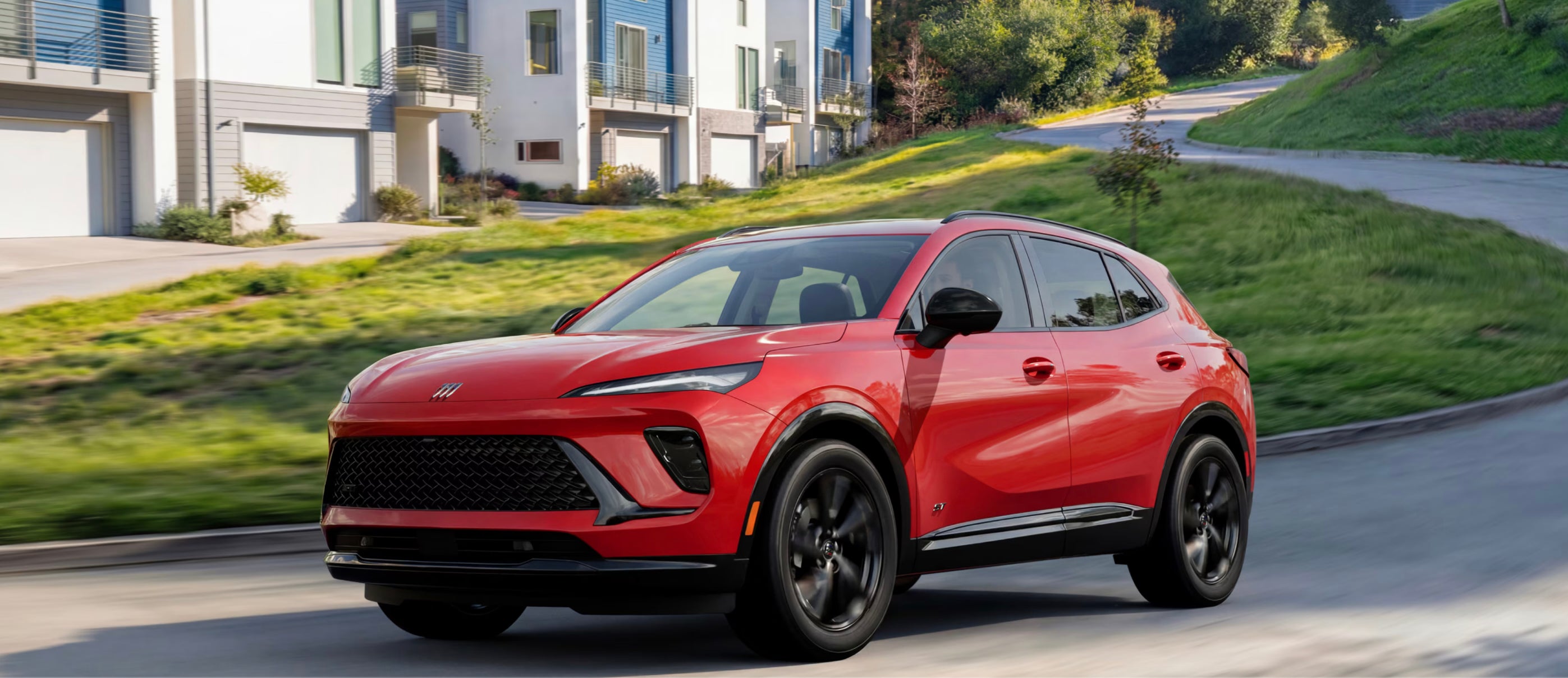 A red 2026 Buick Envision SUV driving down a hill in a suburban neighborhood