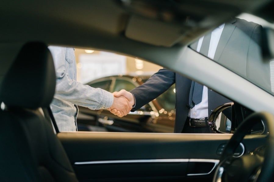 Two people shaking hands, seen through the open side windows of a vehicle